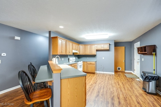 kitchen featuring light brown cabinets, white range with gas stovetop, kitchen peninsula, light hardwood / wood-style floors, and a textured ceiling