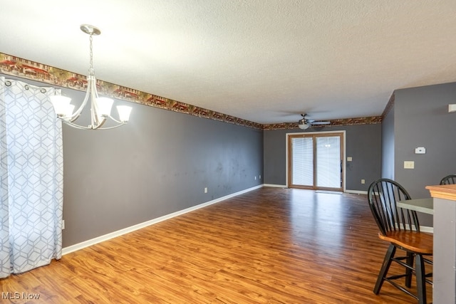 unfurnished dining area featuring a textured ceiling, wood-type flooring, and ceiling fan with notable chandelier