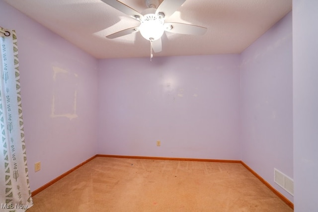 empty room featuring ceiling fan, light colored carpet, and a textured ceiling