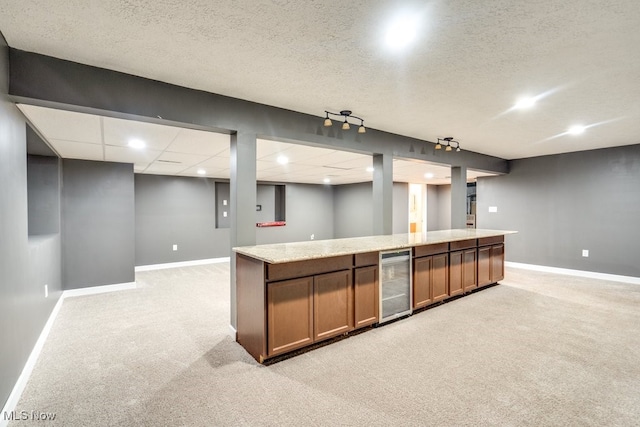 kitchen with light stone countertops, a textured ceiling, light colored carpet, and wine cooler