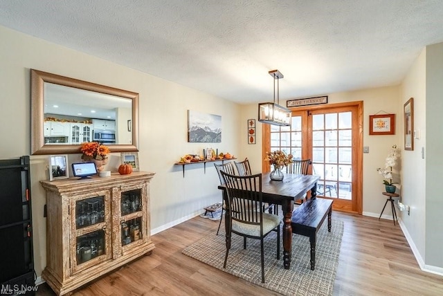 dining room with a textured ceiling, light wood-type flooring, and an inviting chandelier