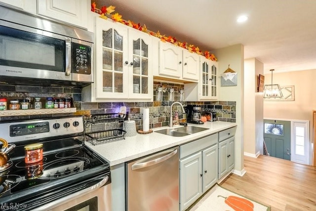 kitchen featuring sink, light wood-type flooring, decorative light fixtures, white cabinetry, and stainless steel appliances