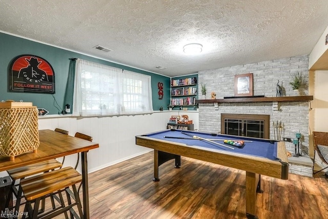 playroom featuring crown molding, a brick fireplace, a textured ceiling, pool table, and wood-type flooring