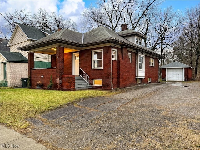 bungalow-style home with entry steps, a detached garage, an outdoor structure, a front lawn, and brick siding