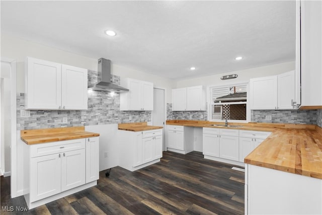 kitchen with white cabinetry, sink, wooden counters, and wall chimney range hood