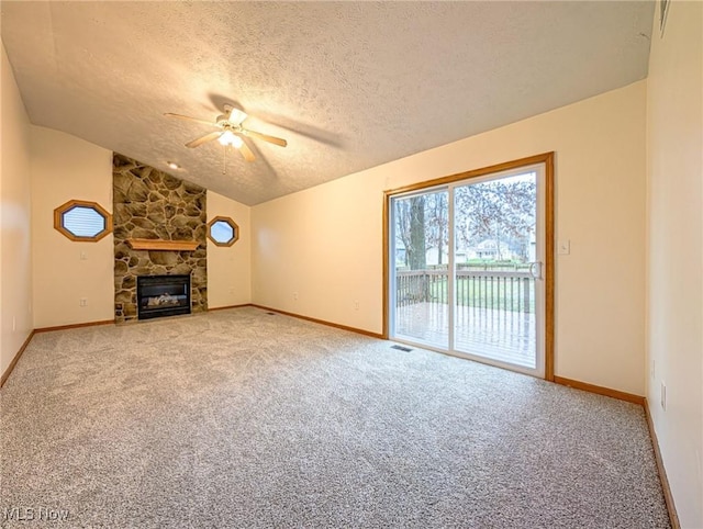 unfurnished living room with a textured ceiling, vaulted ceiling, ceiling fan, a fireplace, and carpet floors