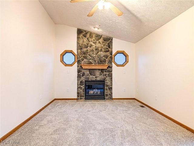 unfurnished living room featuring ceiling fan, a stone fireplace, vaulted ceiling, a textured ceiling, and carpet