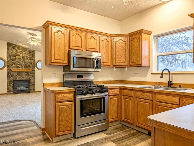 kitchen with sink, ceiling fan, a fireplace, appliances with stainless steel finishes, and light colored carpet