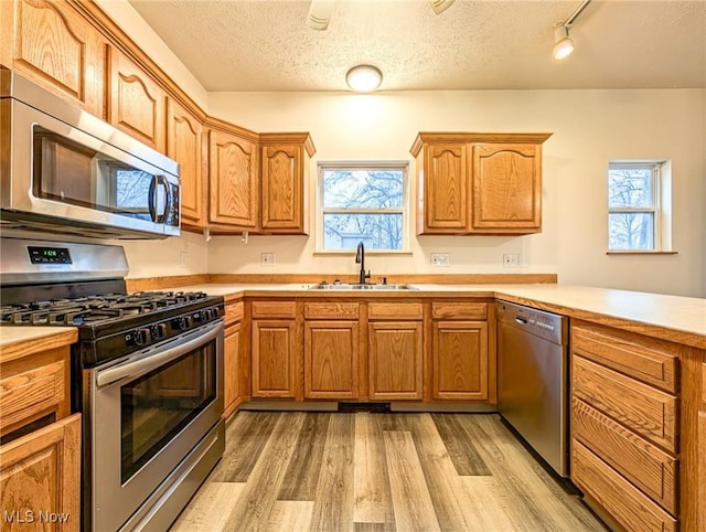 kitchen with a textured ceiling, sink, appliances with stainless steel finishes, and light hardwood / wood-style flooring