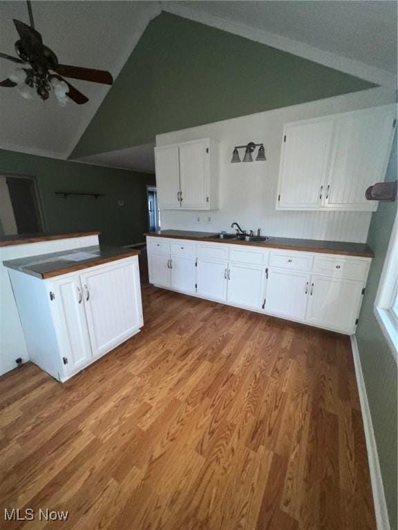 kitchen with white cabinetry, sink, ceiling fan, vaulted ceiling, and light wood-type flooring