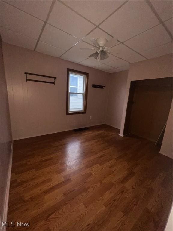 empty room with a drop ceiling, ceiling fan, and dark wood-type flooring