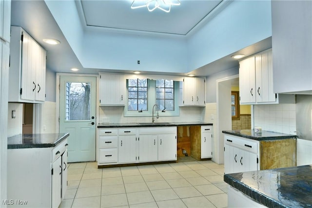 kitchen featuring decorative backsplash, white cabinetry, sink, and light tile patterned floors