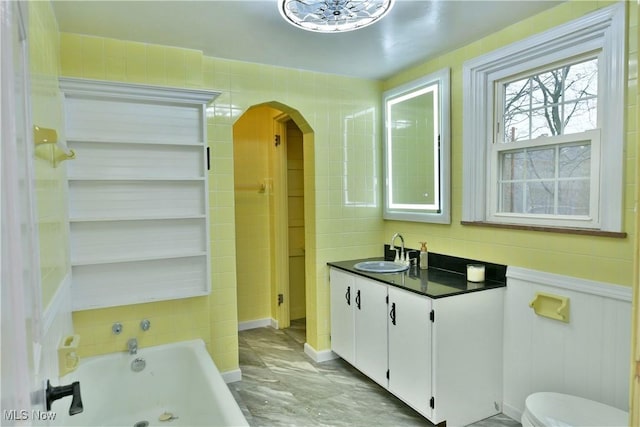 bathroom featuring a bathing tub, ceiling fan, vanity, and toilet