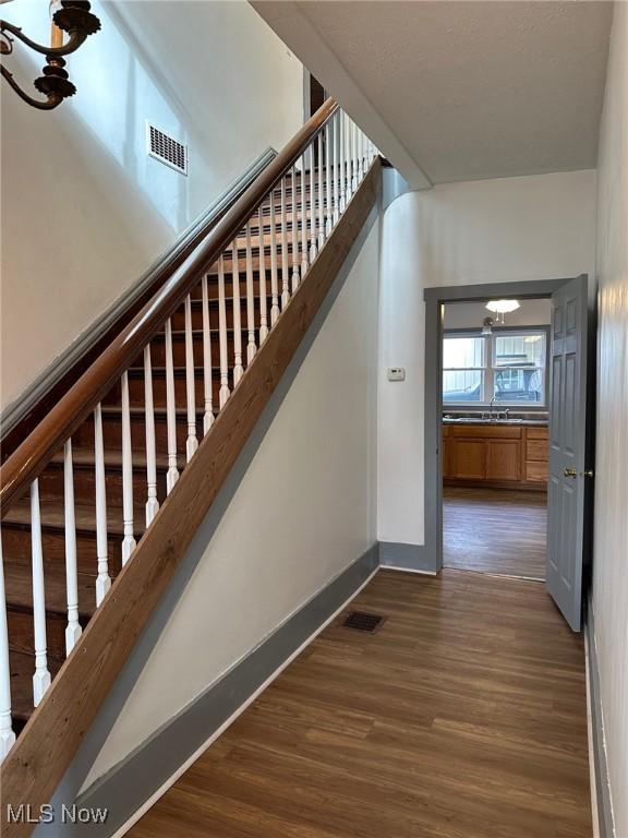 stairway with wood-type flooring and an inviting chandelier