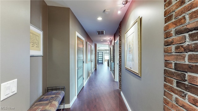 hallway featuring dark wood-type flooring and brick wall