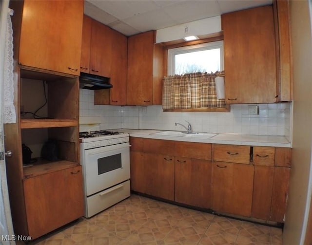 kitchen with a paneled ceiling, backsplash, white gas stove, and sink