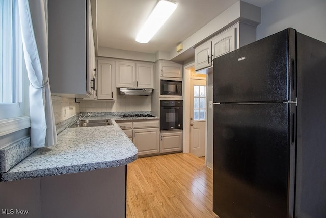 kitchen featuring backsplash, sink, black appliances, and light hardwood / wood-style flooring