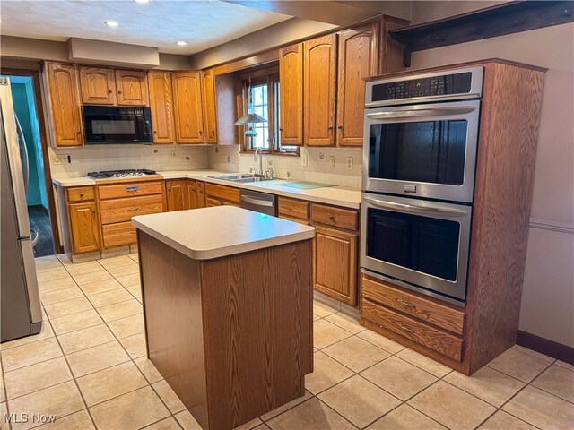 kitchen with backsplash, appliances with stainless steel finishes, a sink, light countertops, and light tile patterned flooring