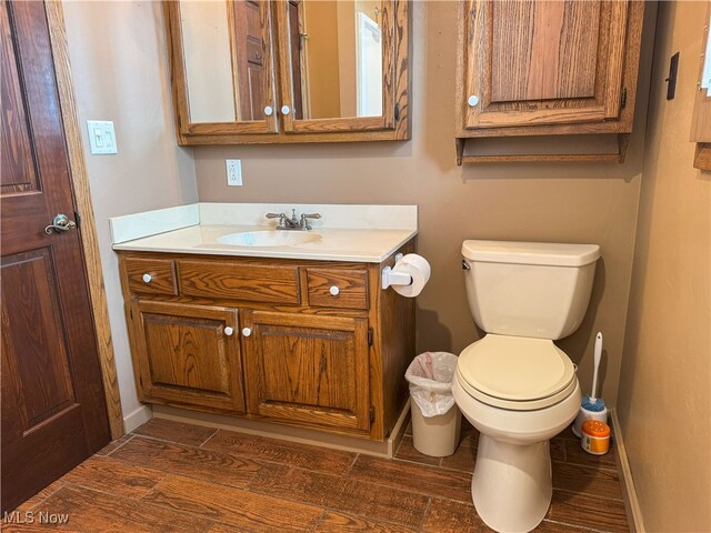 bathroom with toilet, baseboards, wood finished floors, and vanity