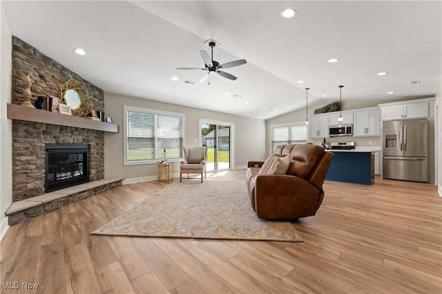 living room with ceiling fan, light hardwood / wood-style floors, a stone fireplace, and vaulted ceiling