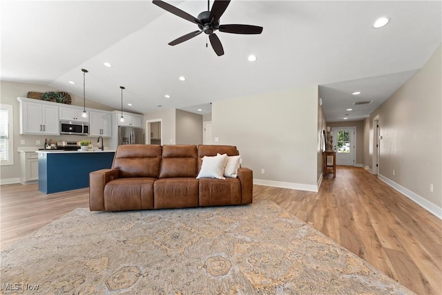 living room with ceiling fan, light wood-type flooring, sink, and vaulted ceiling