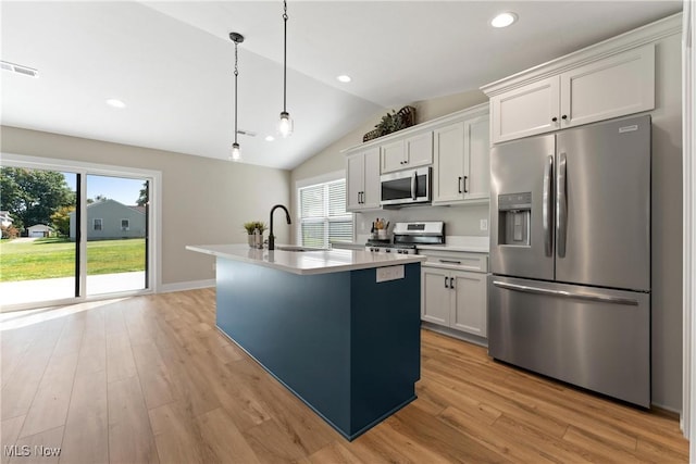 kitchen with an island with sink, white cabinets, hanging light fixtures, and appliances with stainless steel finishes