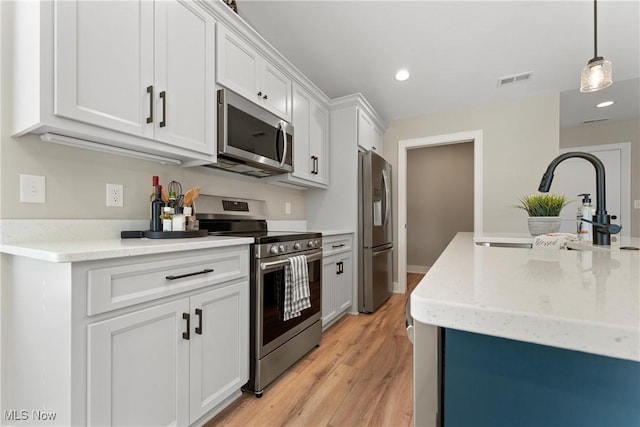 kitchen with stainless steel appliances, sink, light hardwood / wood-style flooring, white cabinetry, and hanging light fixtures