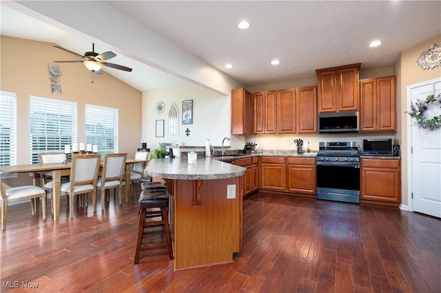 kitchen featuring kitchen peninsula, appliances with stainless steel finishes, a kitchen breakfast bar, dark hardwood / wood-style floors, and lofted ceiling