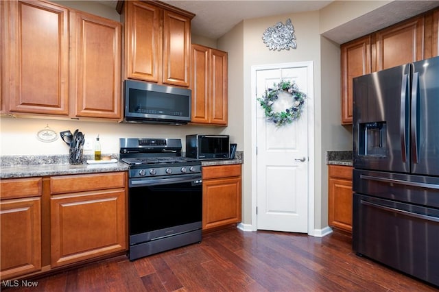 kitchen featuring appliances with stainless steel finishes, dark hardwood / wood-style floors, and dark stone counters