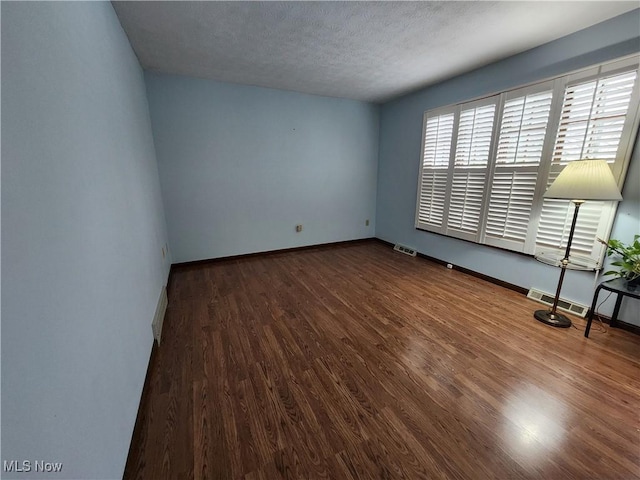 empty room with visible vents, baseboards, a textured ceiling, and wood finished floors