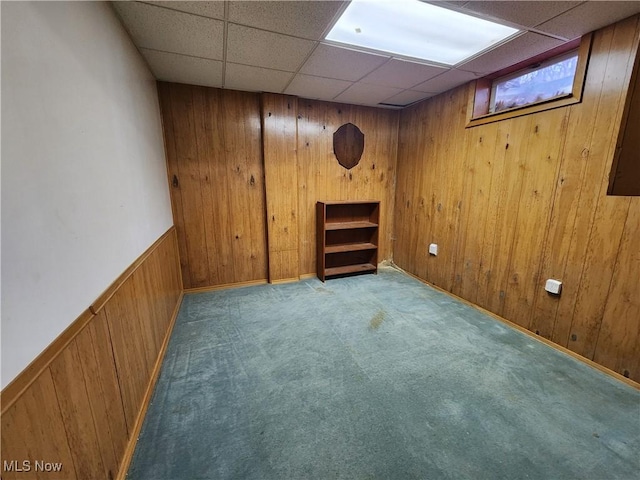 basement with carpet flooring, a paneled ceiling, and wood walls