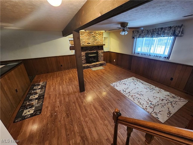 living room featuring ceiling fan, wood walls, hardwood / wood-style floors, a textured ceiling, and a fireplace