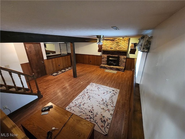 living room with a fireplace, hardwood / wood-style floors, ceiling fan, and wooden walls