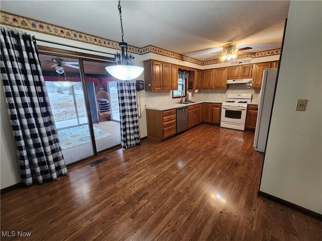 kitchen with decorative backsplash, white appliances, a healthy amount of sunlight, dark wood-type flooring, and hanging light fixtures