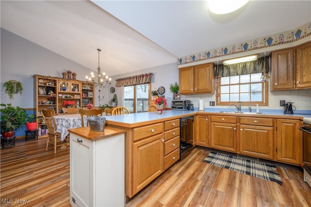 kitchen with kitchen peninsula, vaulted ceiling, sink, dishwasher, and hanging light fixtures