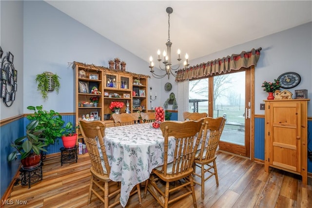 dining room featuring a chandelier, wood-type flooring, vaulted ceiling, and wooden walls