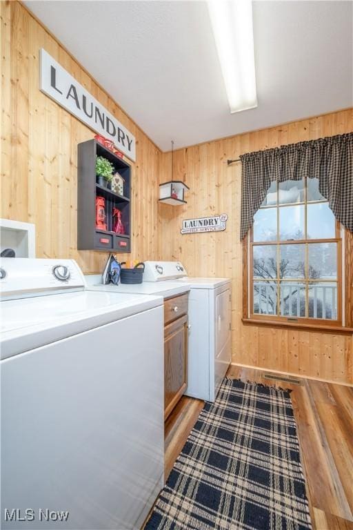 clothes washing area featuring cabinets, wood-type flooring, separate washer and dryer, and wooden walls