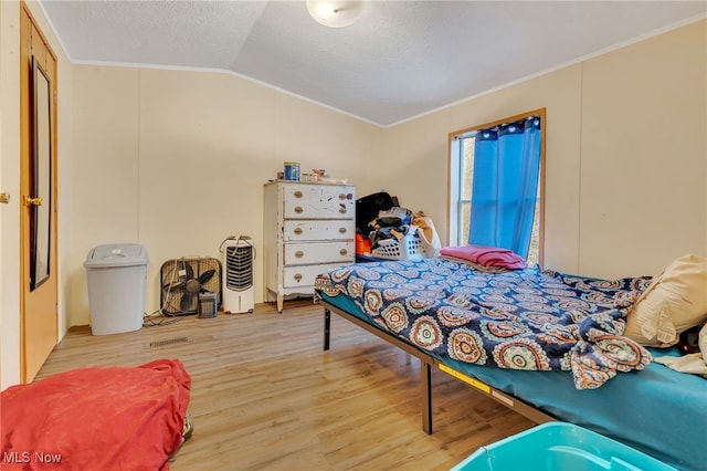 bedroom featuring hardwood / wood-style flooring, ornamental molding, a textured ceiling, and vaulted ceiling