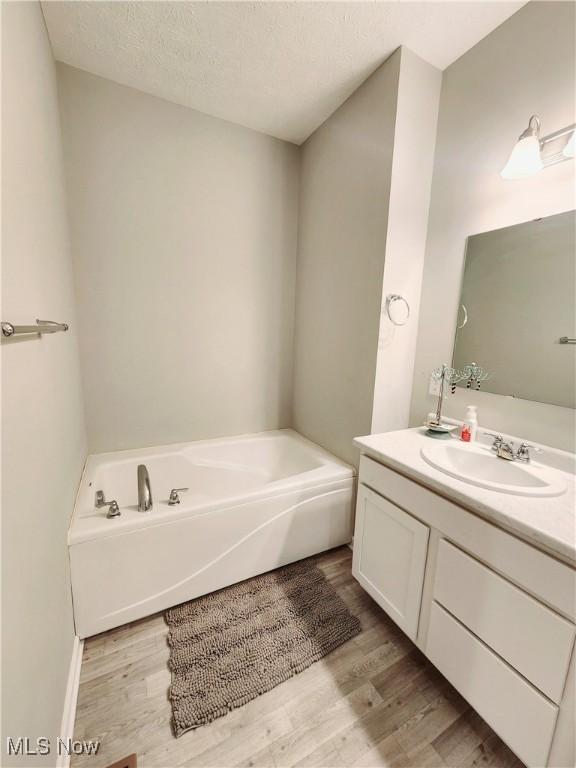 bathroom with hardwood / wood-style flooring, vanity, a tub, and a textured ceiling