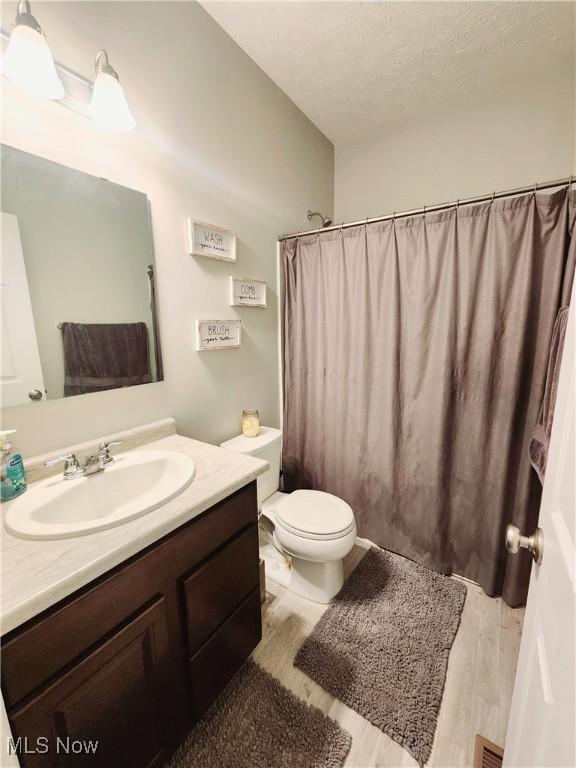 bathroom with hardwood / wood-style flooring, vanity, toilet, and a textured ceiling