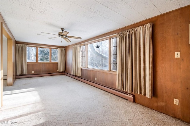 carpeted empty room with wood walls, ceiling fan, and a baseboard radiator