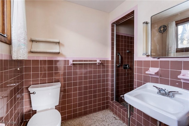 bathroom featuring tiled shower, toilet, tile walls, and sink