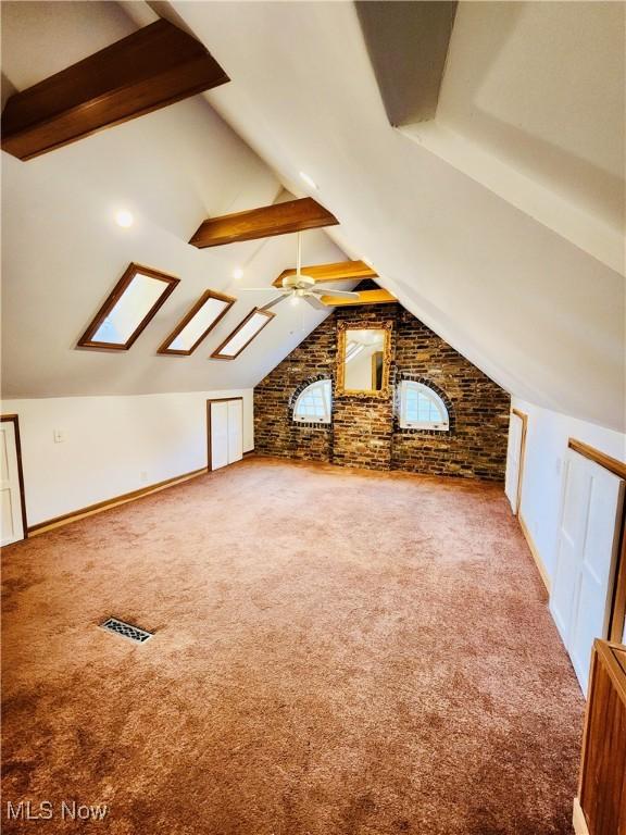 bonus room with carpet flooring, ceiling fan, vaulted ceiling with skylight, and brick wall