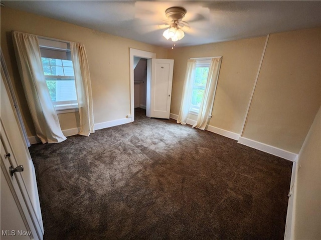 unfurnished bedroom with multiple windows, ceiling fan, and dark colored carpet