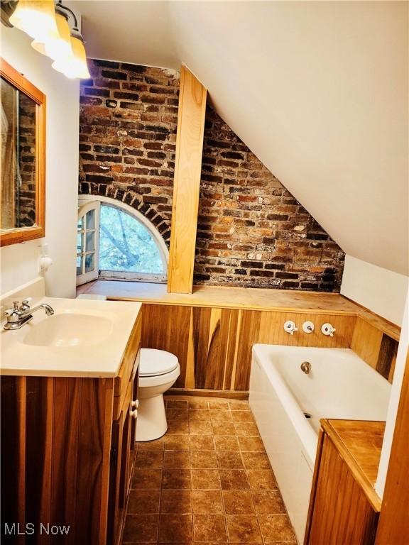 bathroom featuring brick wall, a washtub, vanity, vaulted ceiling, and toilet