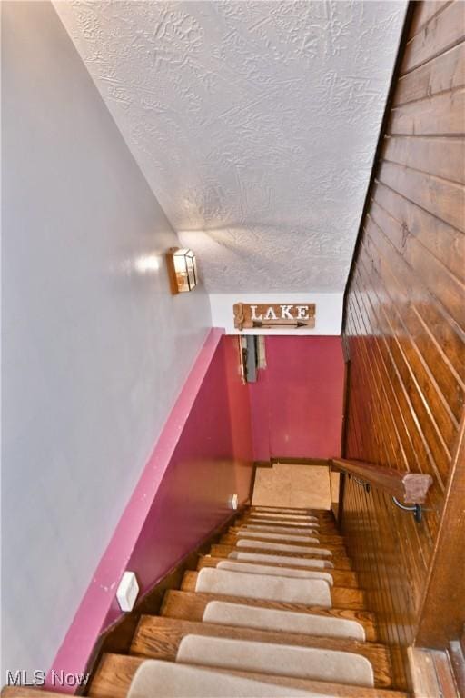 stairway featuring a textured ceiling and wooden walls