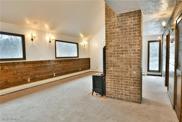 interior space with a wood stove, light carpet, wooden walls, vaulted ceiling, and baseboard heating