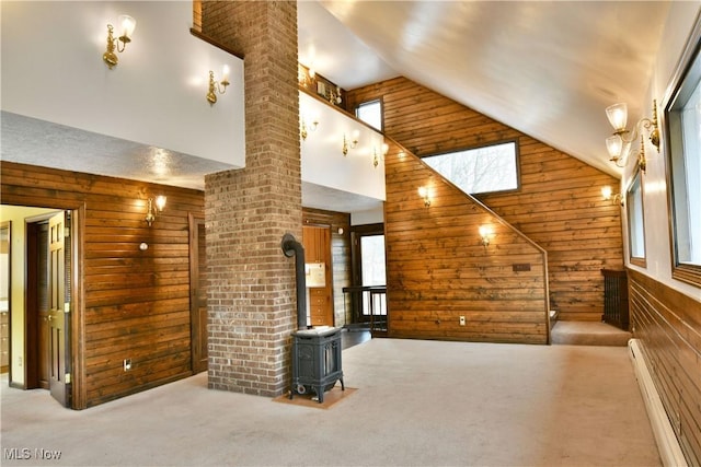 unfurnished living room featuring a wood stove, a baseboard radiator, light carpet, high vaulted ceiling, and wooden walls