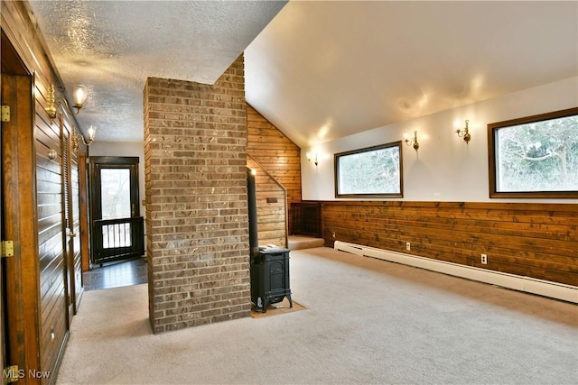 additional living space with wood walls, lofted ceiling, a wood stove, light carpet, and a baseboard radiator