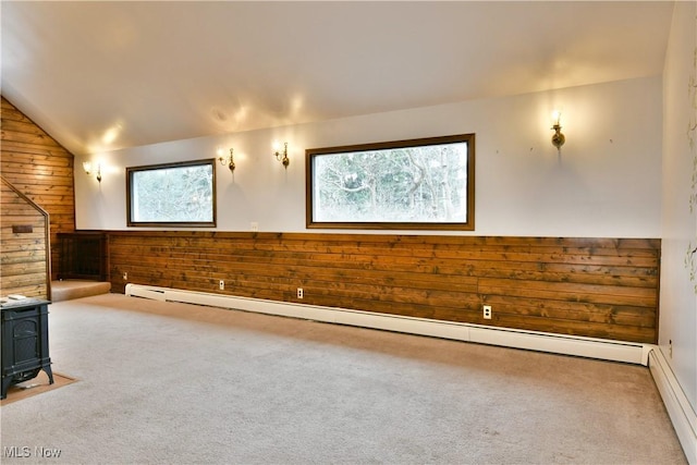 carpeted spare room featuring lofted ceiling, a wood stove, wooden walls, and a baseboard radiator